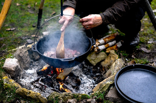 Person bereitet ein Gericht im Kazan über einem offenen Feuer in der Natur zu
