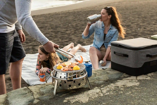 Eine Familie genießt gemeinsam die Zeit am Strand und grillt auf einem Atago-Gasgrill