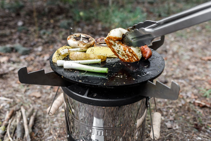 Fleisch und buntes Gemüse auf einer heißen Grillplatte über einem Raketenofen gegart