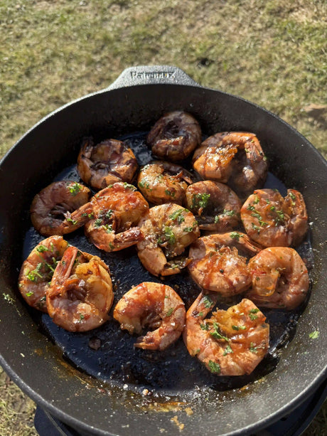 Garnelen in Knoblauchbutter mit Whisky, Orange und frischen Kräutern in einer heißen Gusspfanne, direkt vom Grill serviert
