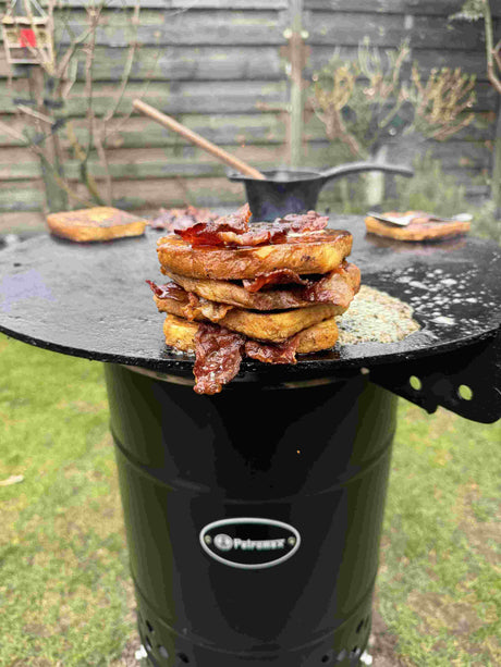 Goldbraun gebratener French Toast mit knusprigem Bacon, Ahornsirup und frischen Waldbeeren auf der Petromax Plancha Grillplatte der Feuertonne Pyron serviert.